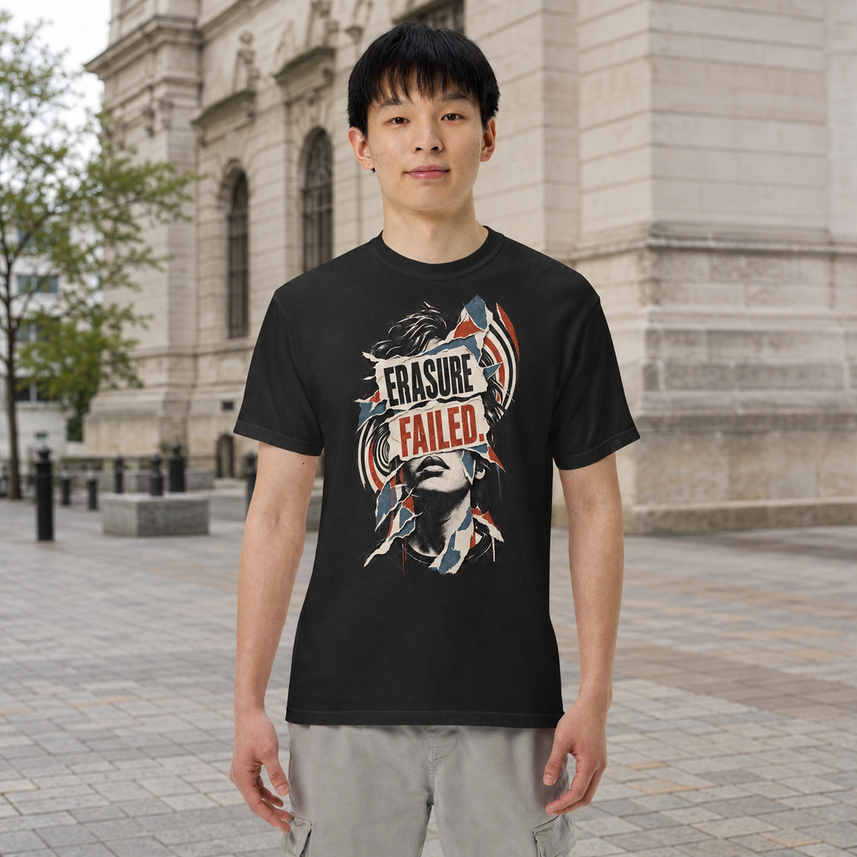 Product visualization: model wearing the black Erasure Failed portrait tee in a city plaza.
