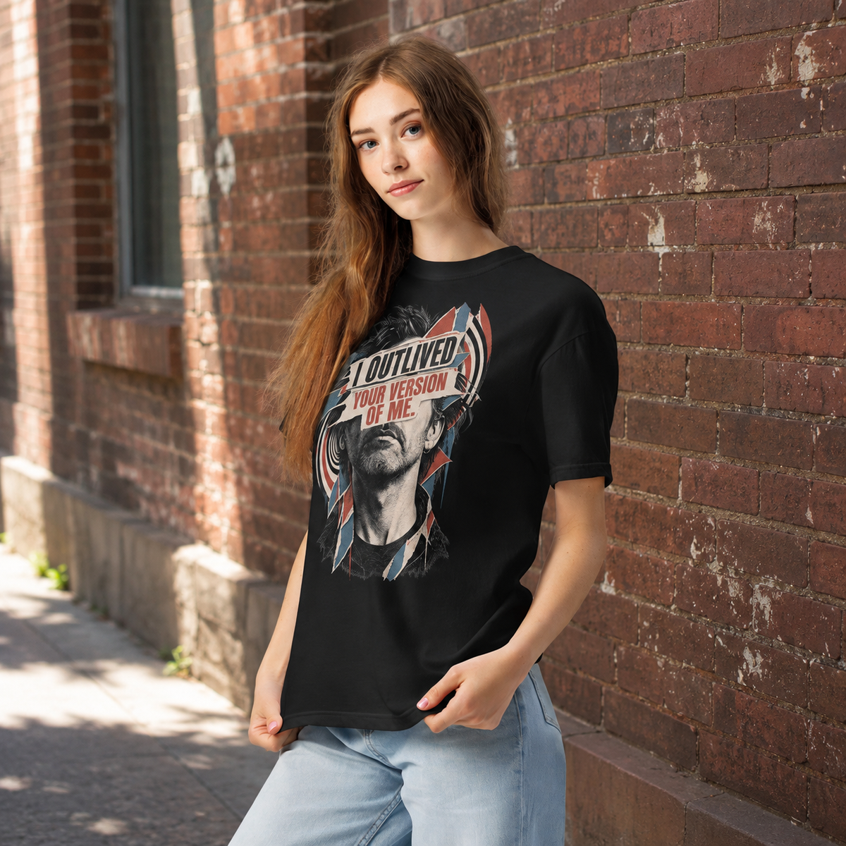 Product visualization: woman wearing the black I Outlived Your Version of Me portrait tee beside a brick wall.