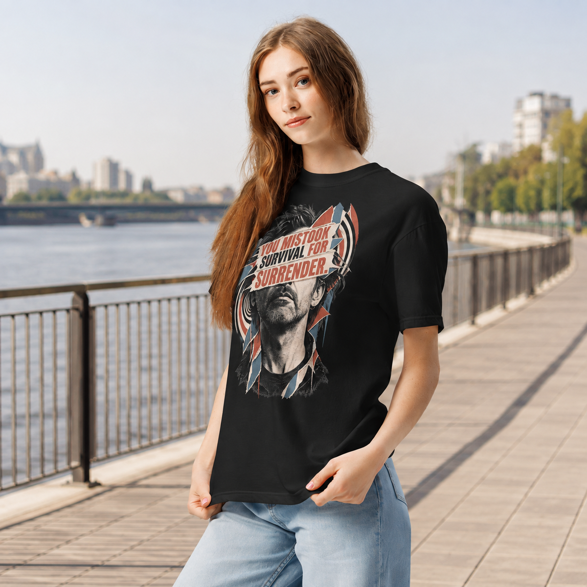 Product visualization: woman wearing the black You Mistook Survival for Surrender portrait tee beside a river walkway.